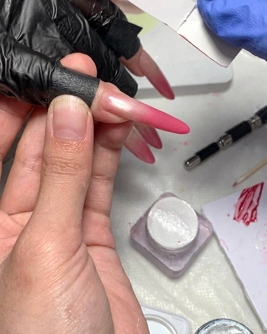 A close-up view of a lint-free wipe being used to clean the skin and edges surrounding a nail with a magenta gradient.