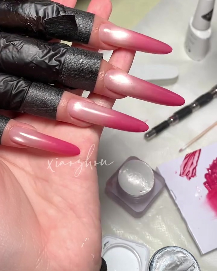 A brush applying a clear, glossy top coat over a magenta magnetic gel nail design.