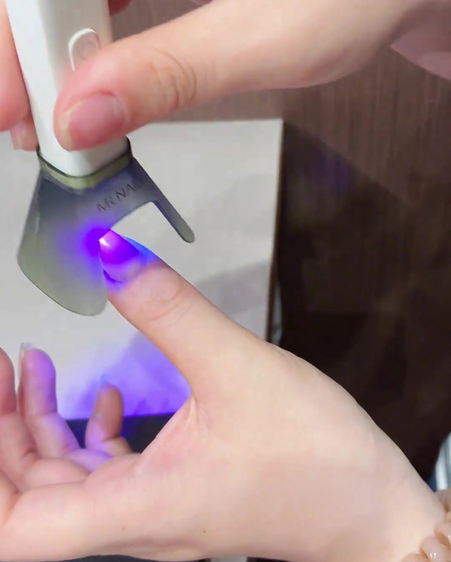 A brush applying a shimmering cat-eye gel polish across the entire surface of a natural nail.