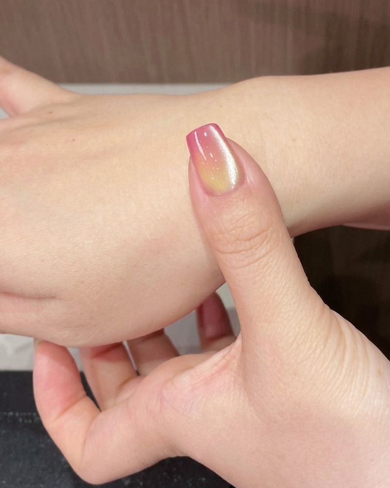 A finger with a shimmering cat-eye gradient nail placed under a portable UV lamp.