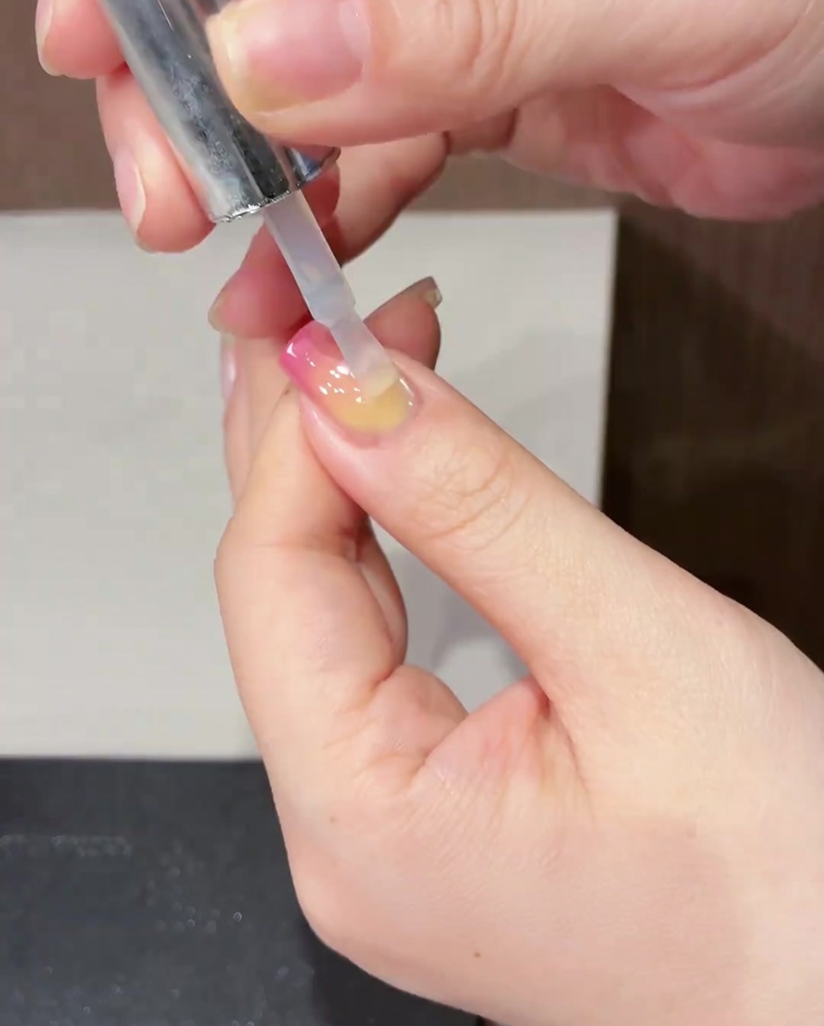 A brush applying a clear, glossy top coat over a finished spring tulip nail design.