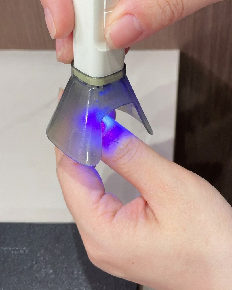A finger being held under a portable UV lamp for the final hardening step of the manicure.