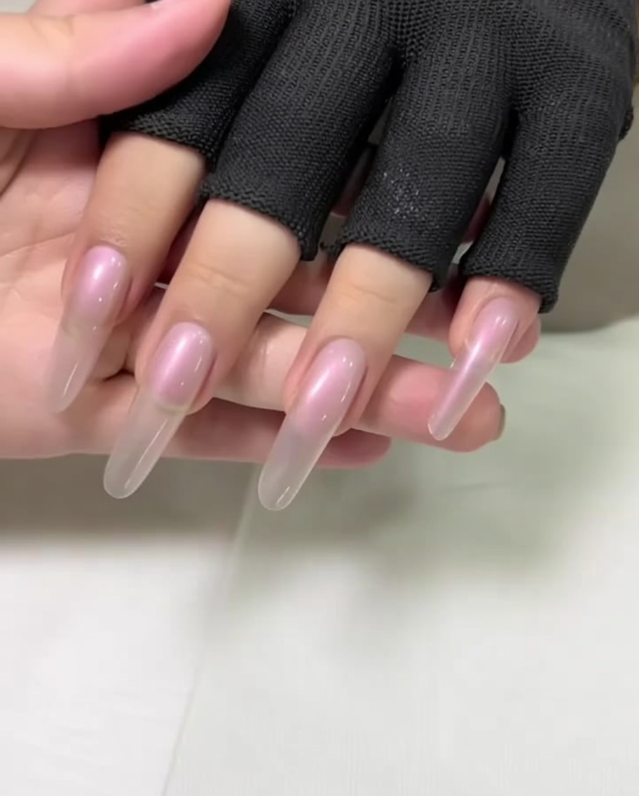 A close-up of a hand with long, almond-shaped nails being prepped by pushing back the cuticles with a metal pusher.