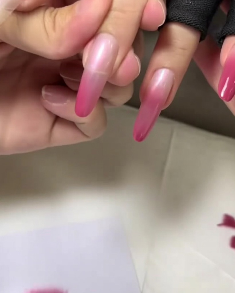 A close-up of the nail tip being dabbed with the final, darkest layer of pink color to finalize the gradient.