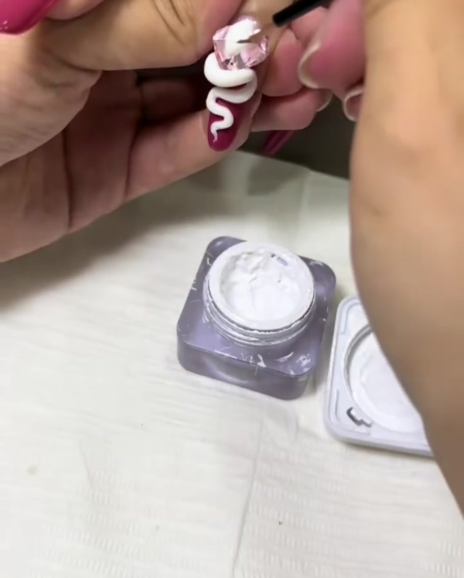A thin detail brush applying white gel to add texture to a 3D snake design on a nail.