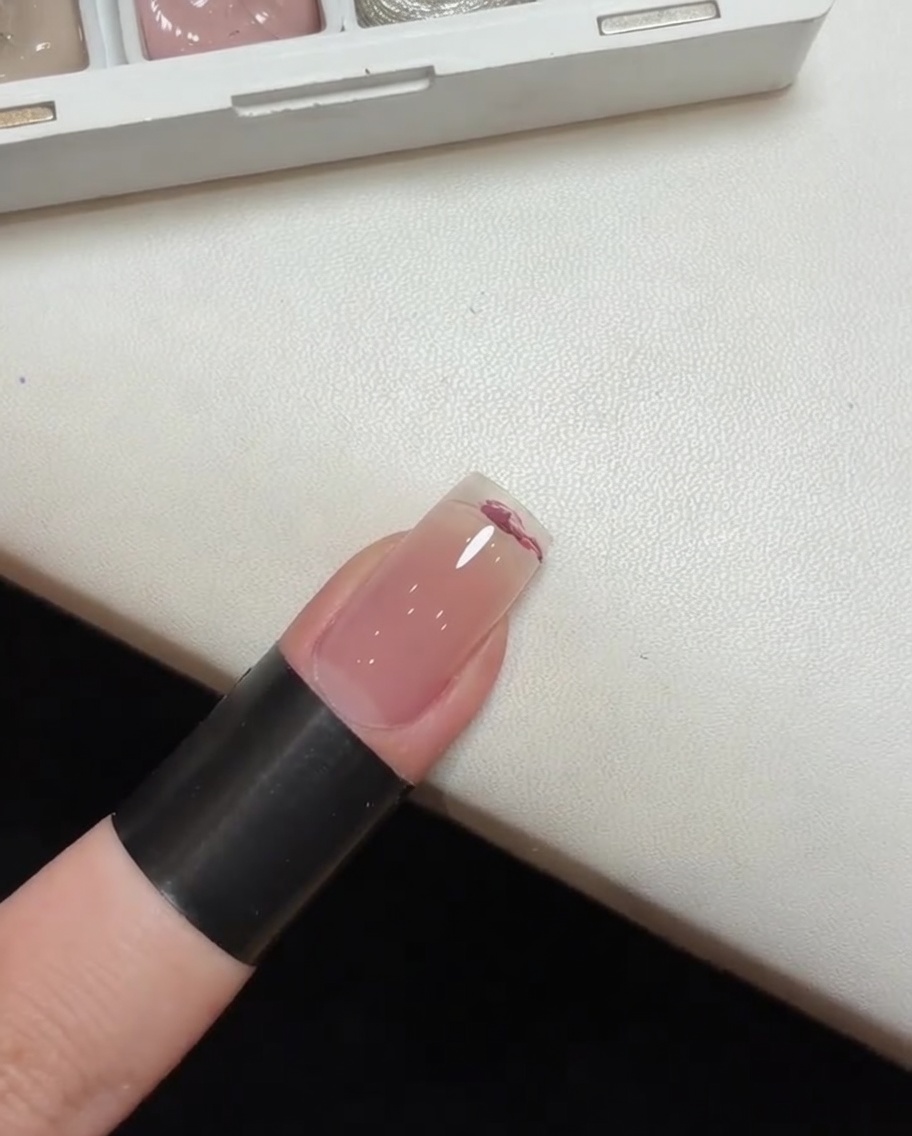 A sponge tool being used to pat and blend pink gel polish on a nail to form a gradient effect.
