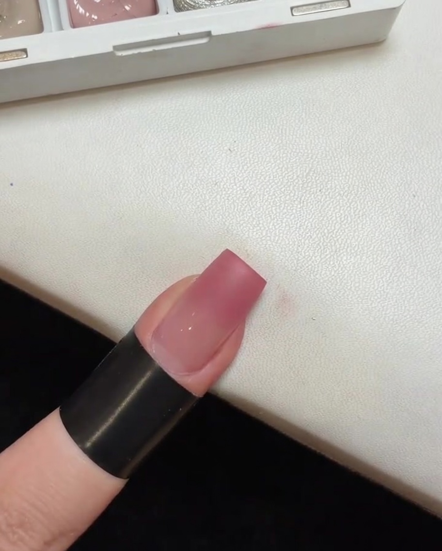 A nail with a pink gradient base curing inside a small portable UV lamp.
