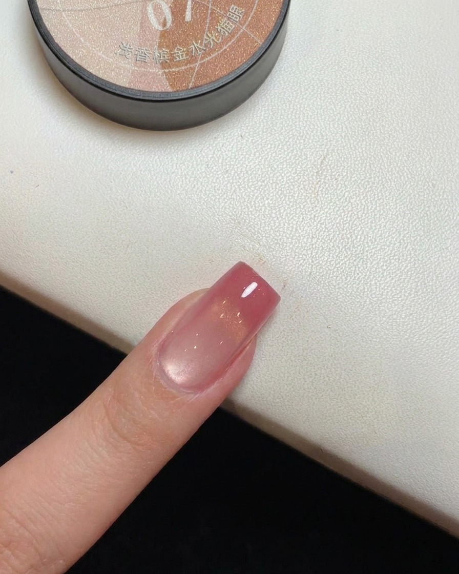 A close-up of a nail with magnetic gold shimmer curing under a UV lamp.