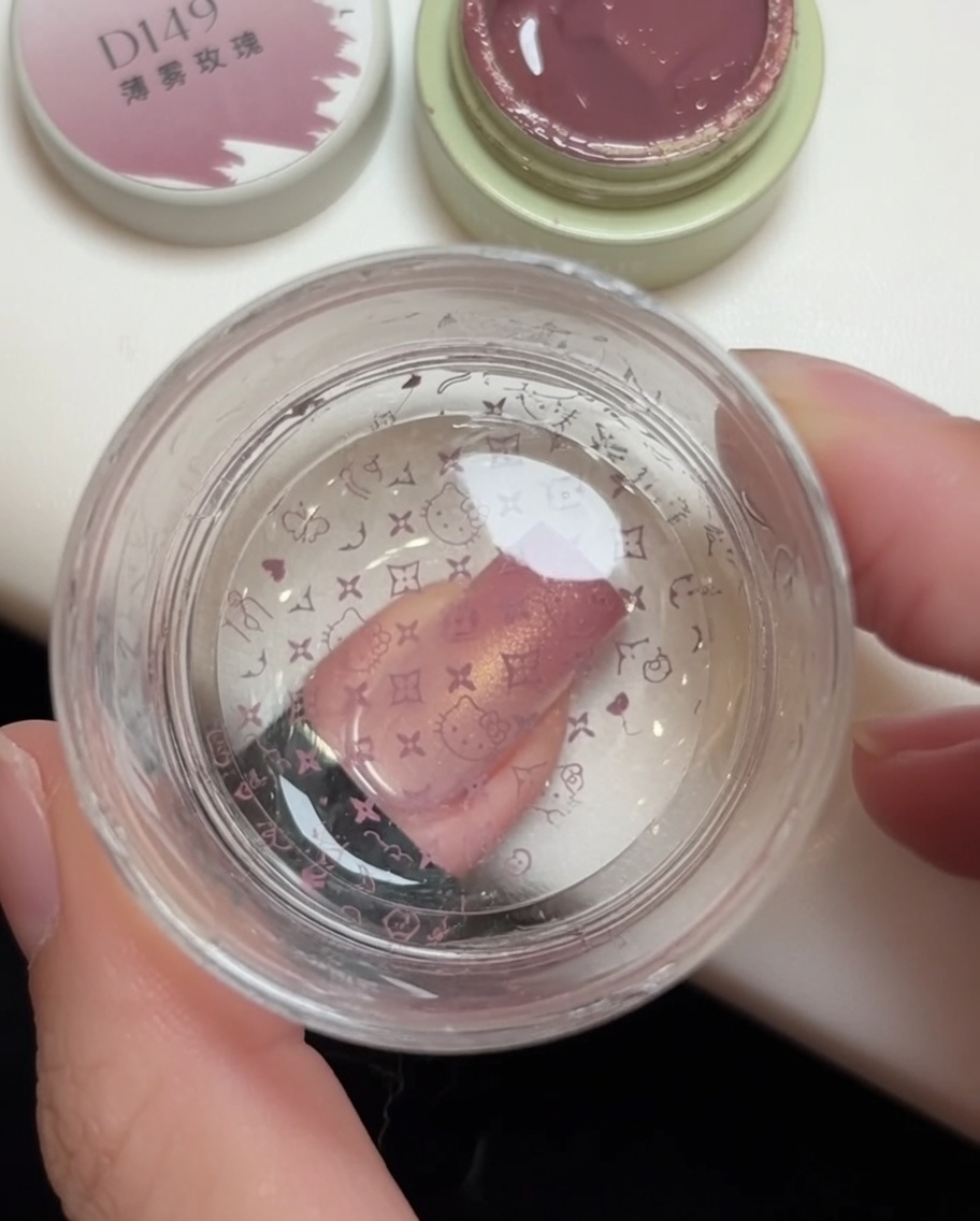 A jelly stamper pressing a pink pattern onto a nail, with the Hello Kitty design visible on the stamper head.