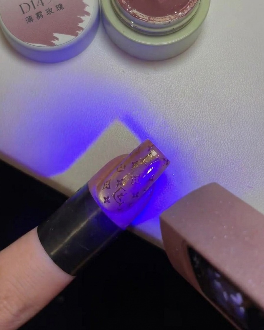 A finger with a stamped Hello Kitty design on the nail held under a purple UV lamp light.
