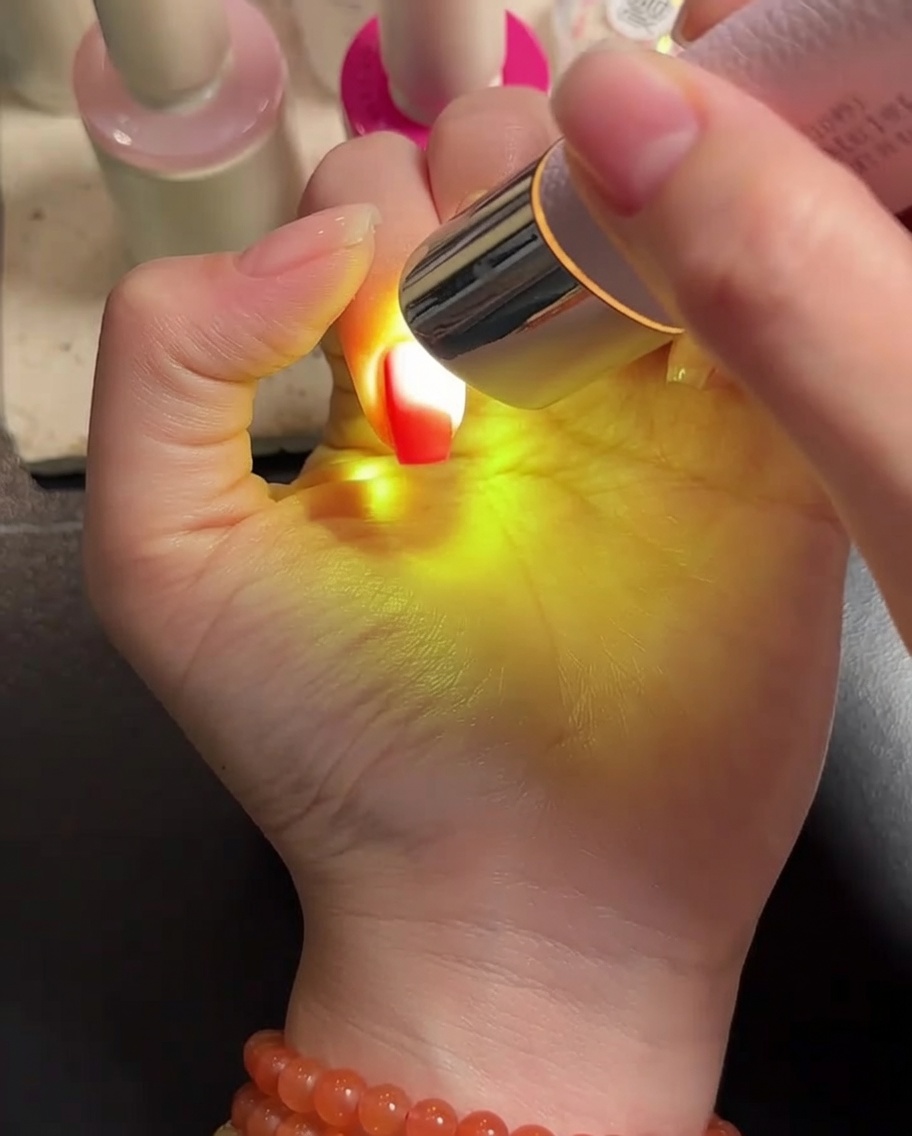 A hand placed under a portable LED lamp, with the gel-coated nails being cured under the bright light.