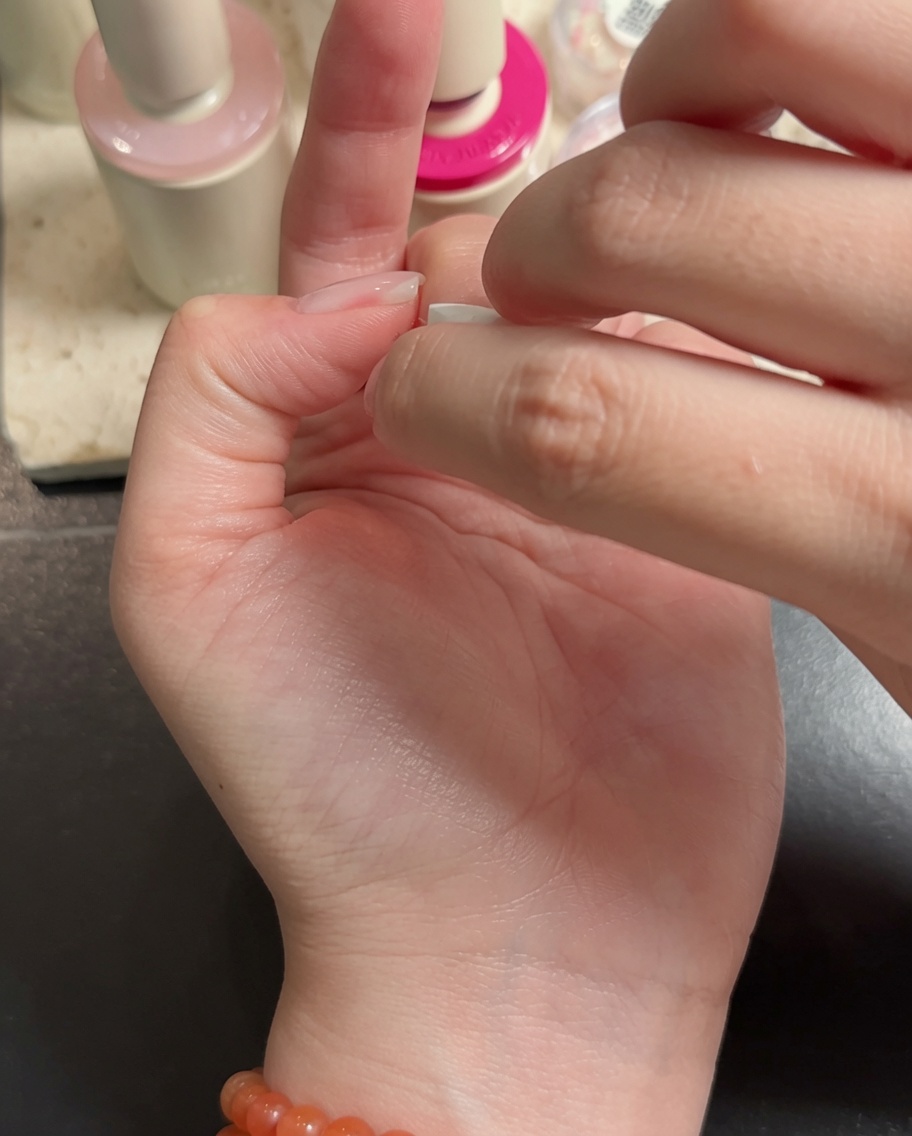 A nail art brush applying white gel to the tips of the middle and ring fingers, creating a gradient effect.