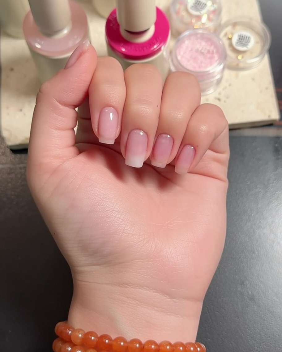 A hand positioned under an LED lamp, curing the freshly applied white gradient on the nails.