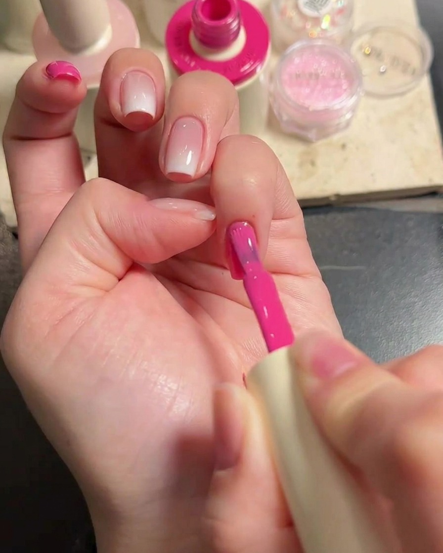 Close-up of a hand with a nail brush applying vibrant pink gel polish to the fingernails.