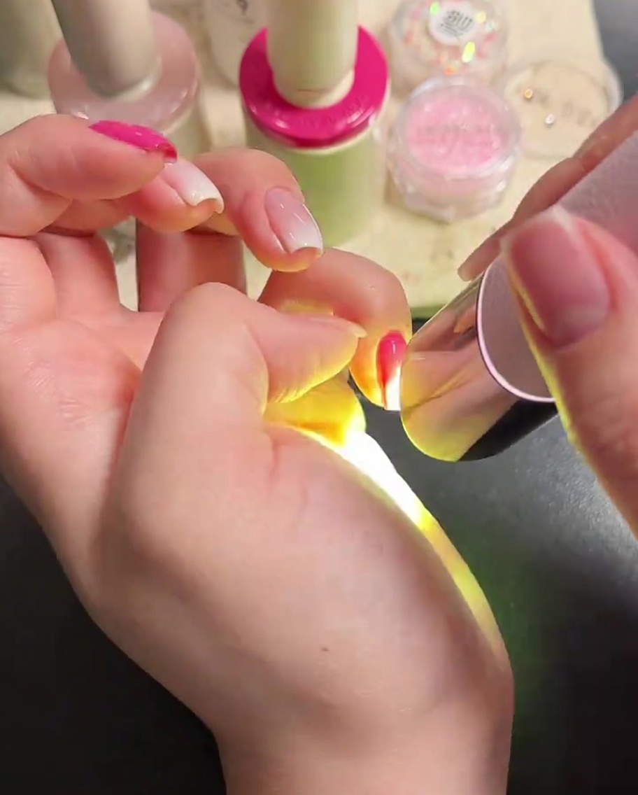 A nail brush applying a clear, glossy top coat to manicured nails.