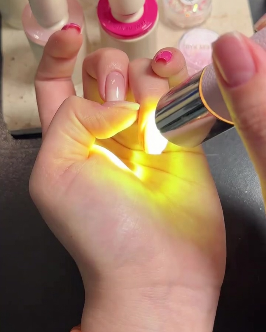 A hand placed under an LED lamp with the fingers clearly visible while curing the top coat.
