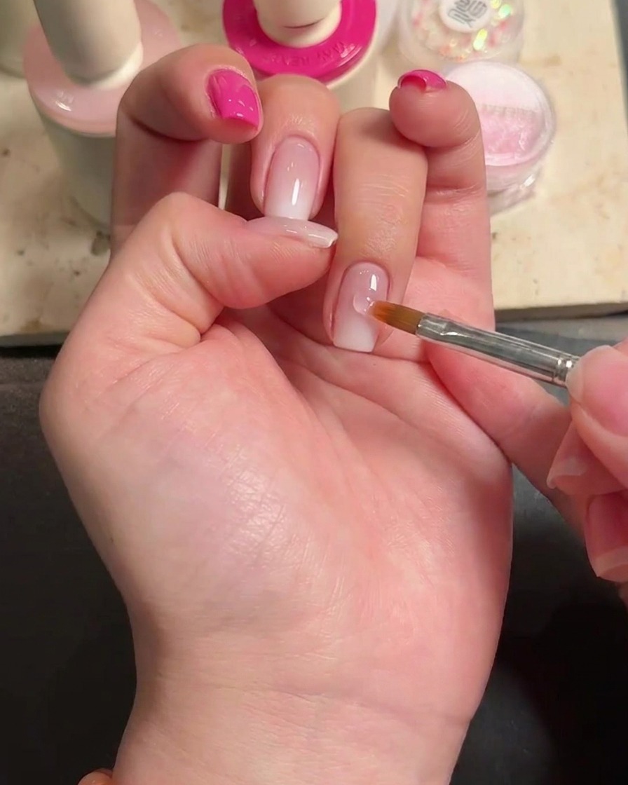 A close-up view showing a drop of nail glue applied to a polished ring finger nail.