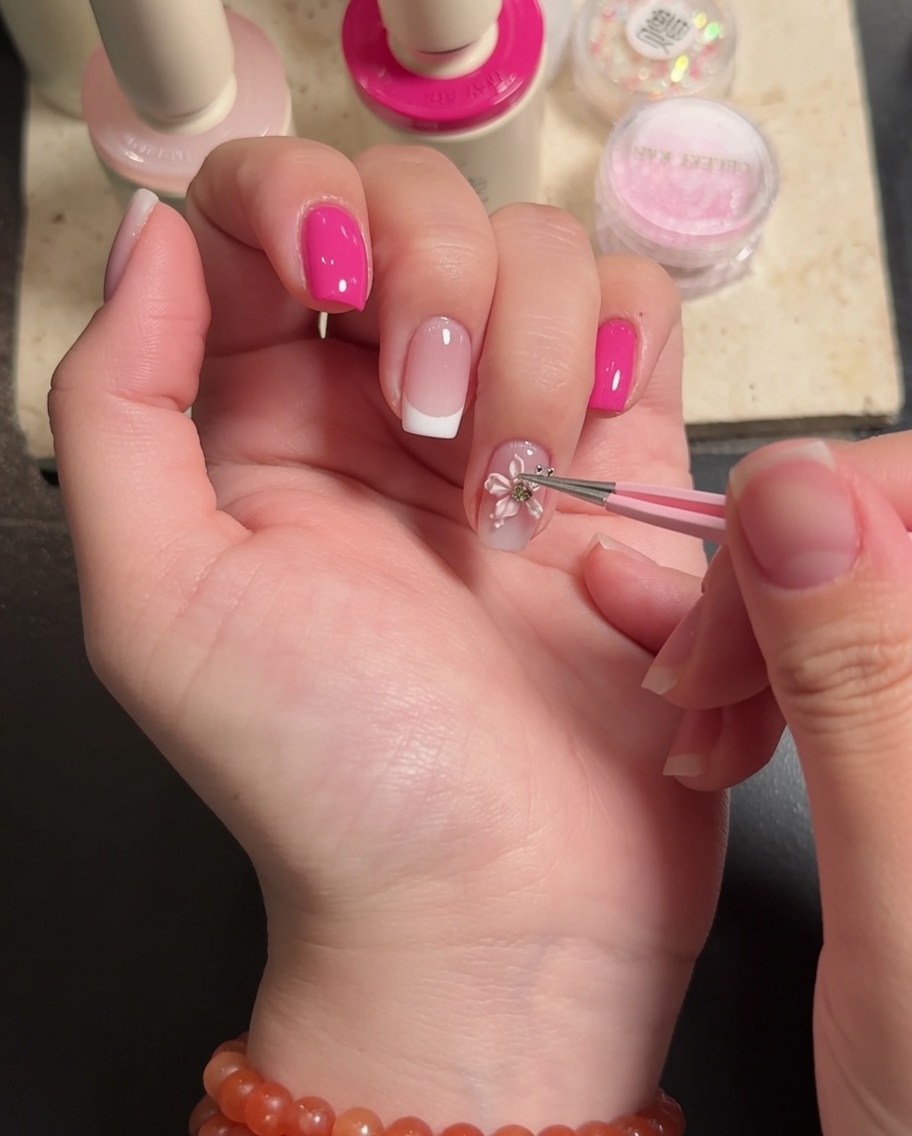 A brush applying a final top coat of clear gel around the edges of a 3D floral nail decoration.