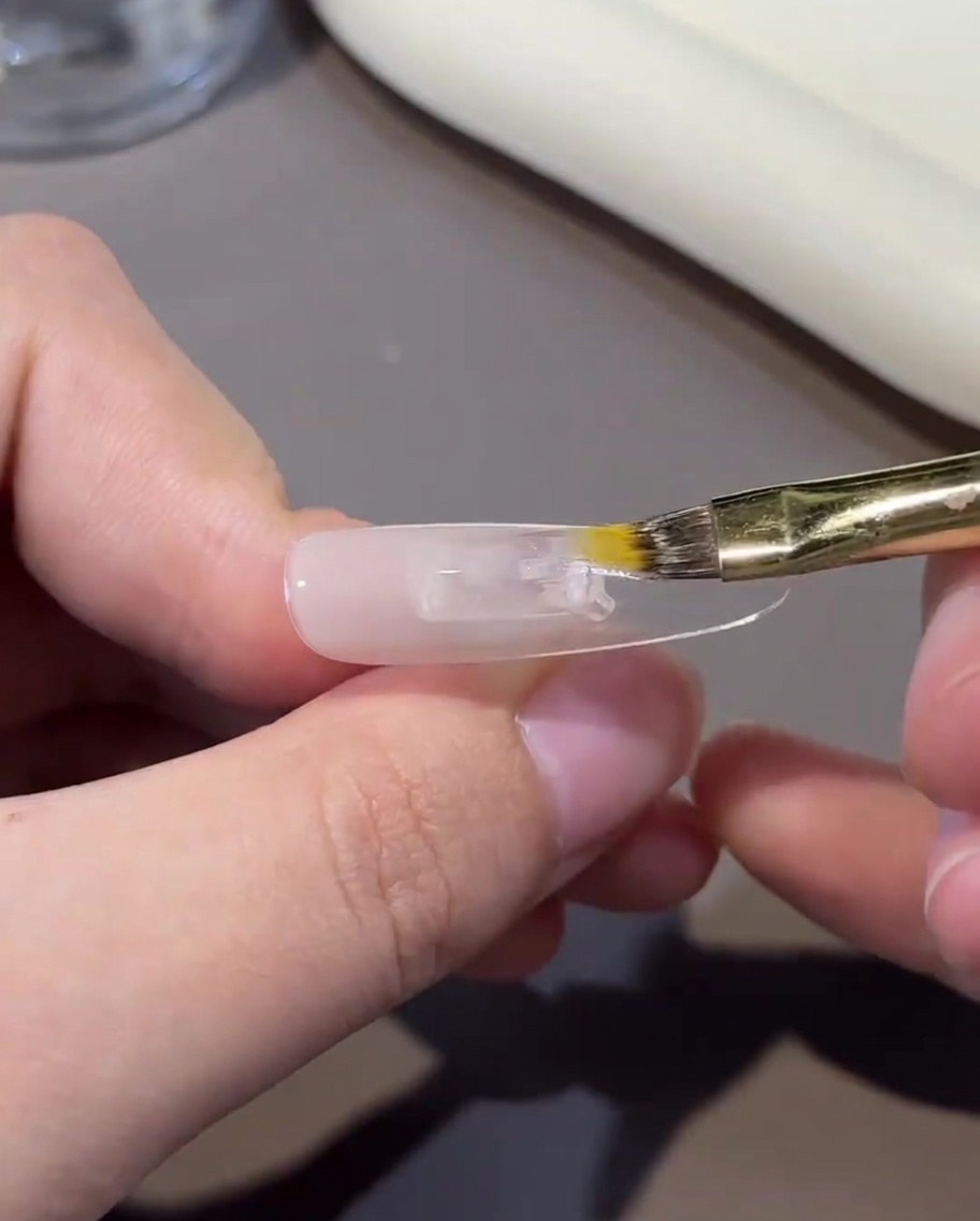 A close-up view of a brush lightly blending the nude gel on the nail surface to create a gradient effect.
