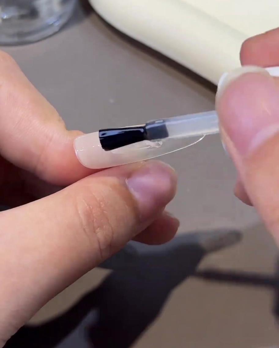 A brush applying a clear, viscous strengthening gel onto the nail, creating a smooth surface.