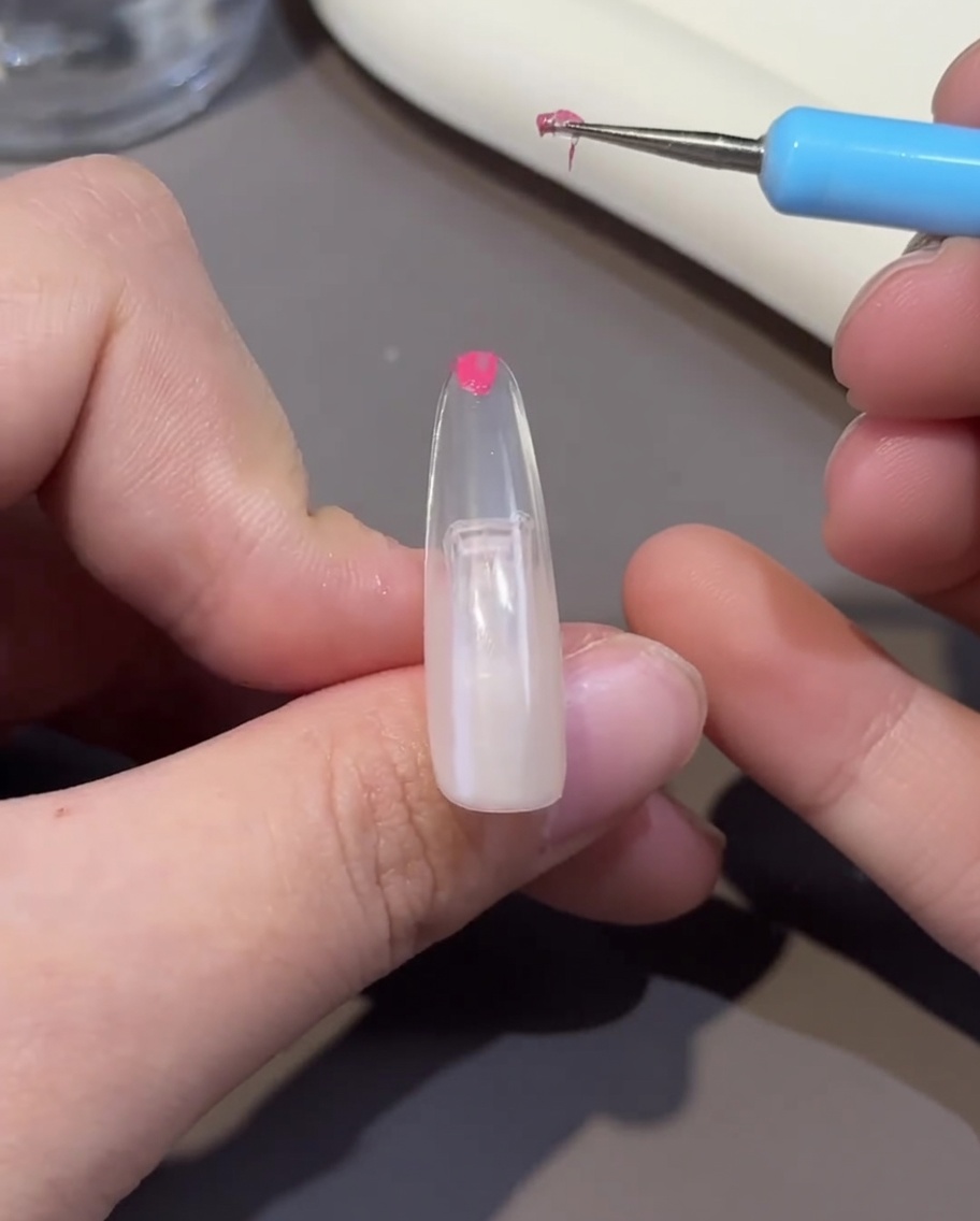 A nail tip being cured under a UV/LED nail lamp, showing the gel surface set.