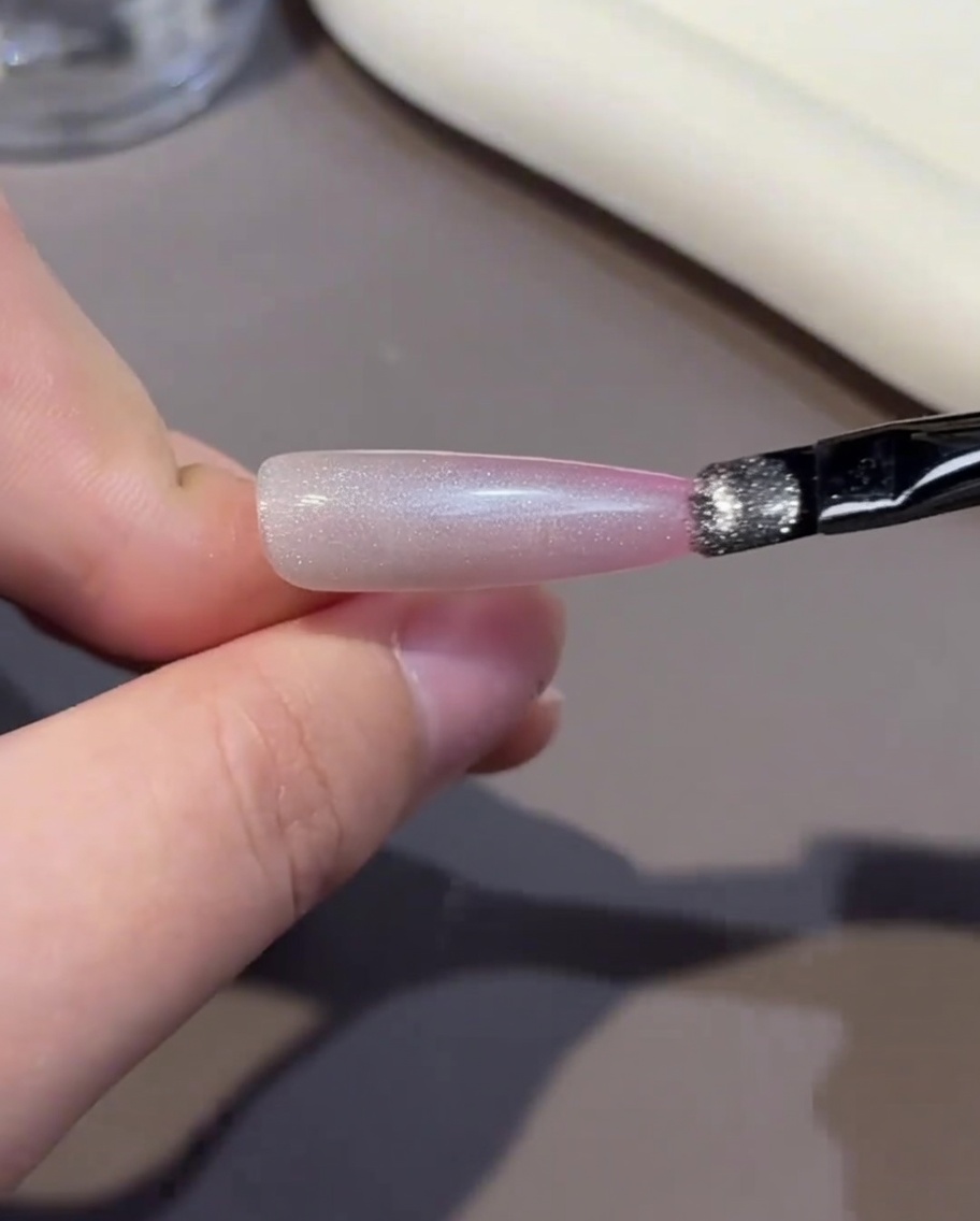 A brush applying a layer of pink gel polish to the tip of a nail.