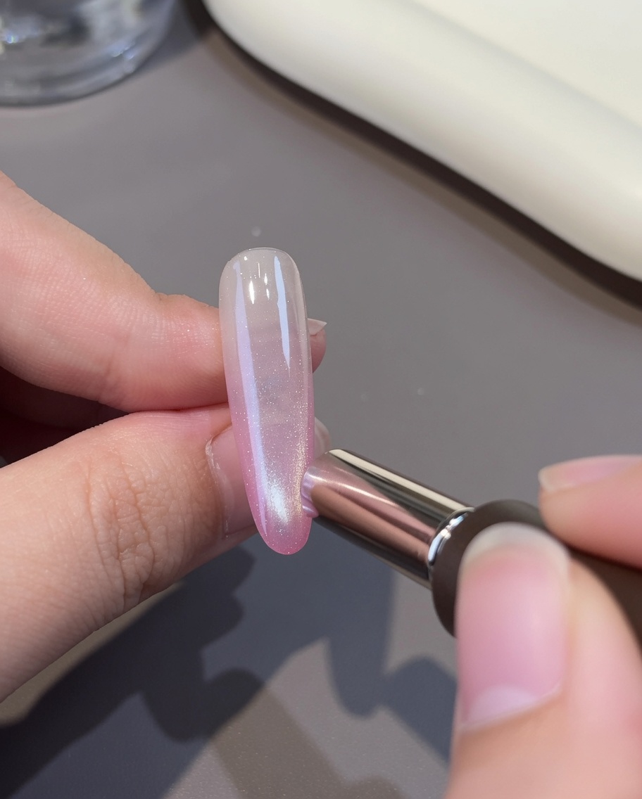 A layer of white cat-eye gel being applied over the pink base on a nail.