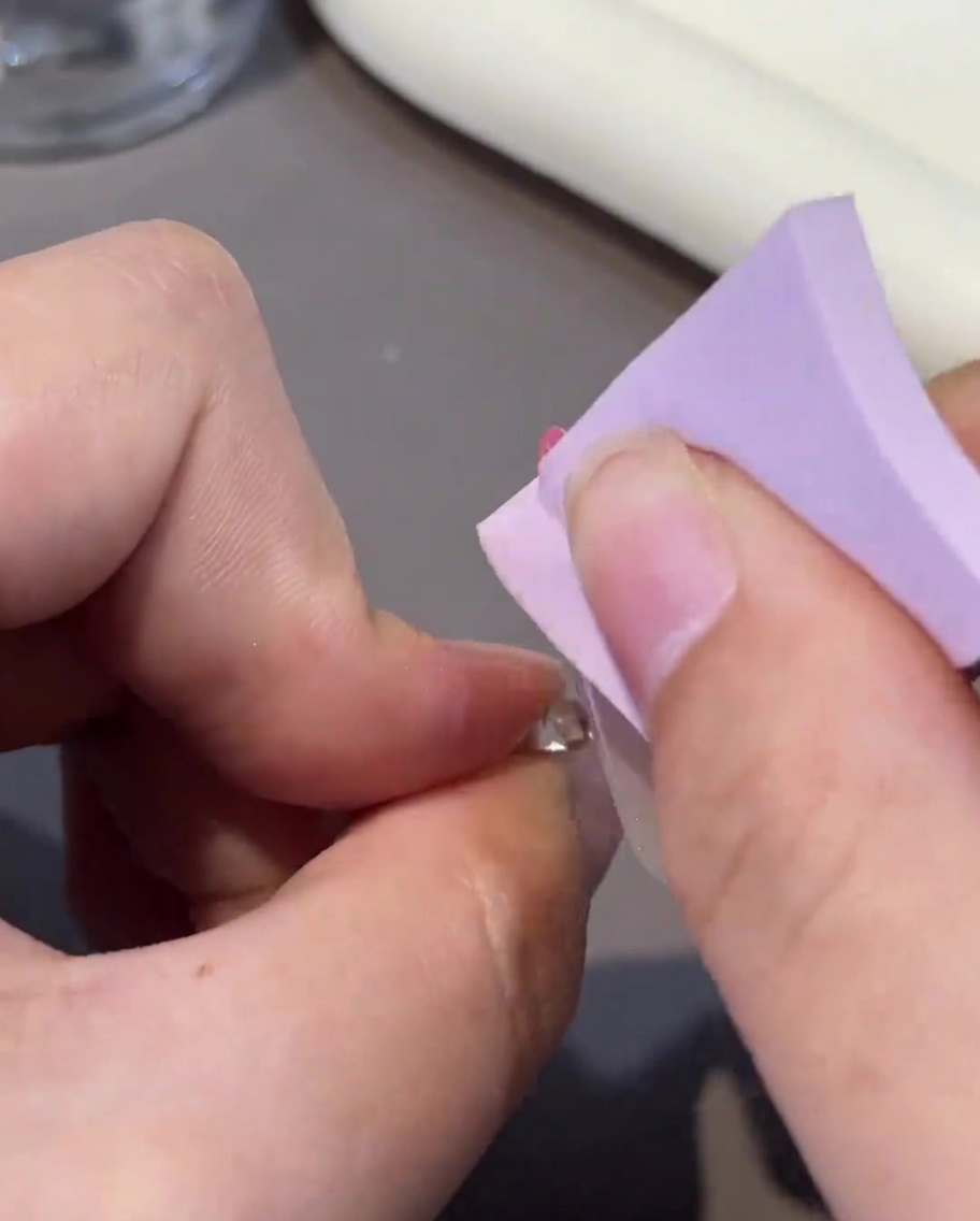 A lint-free wipe being used to clean the surface of a cured gel nail.