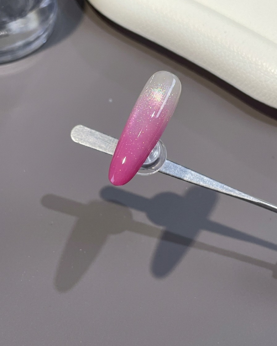 A brush applying a clear, glossy top coat onto a finished pink ombre nail.