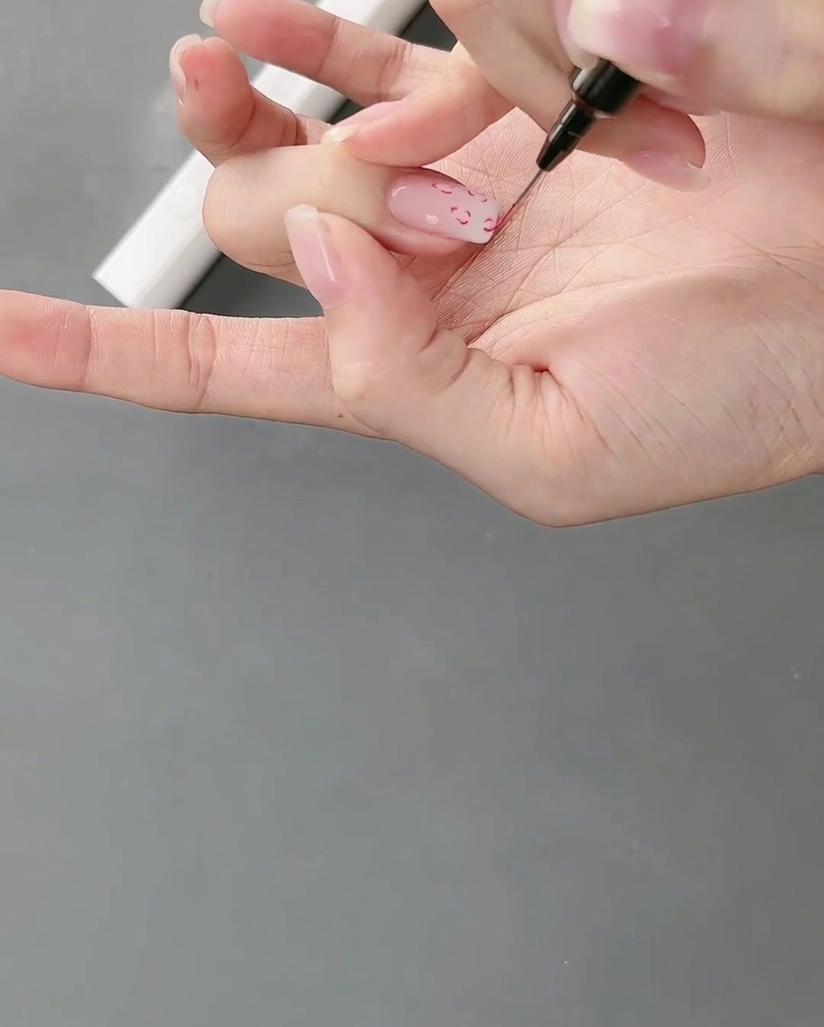 A hand positioned under a nail lamp, curing the freshly painted fine line nail art.