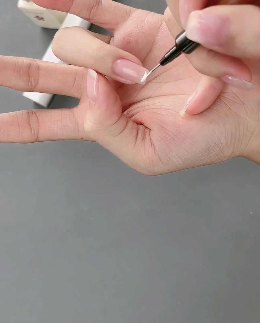 A liner brush applying a precise white gel line to create a high-position French tip on a fingernail.