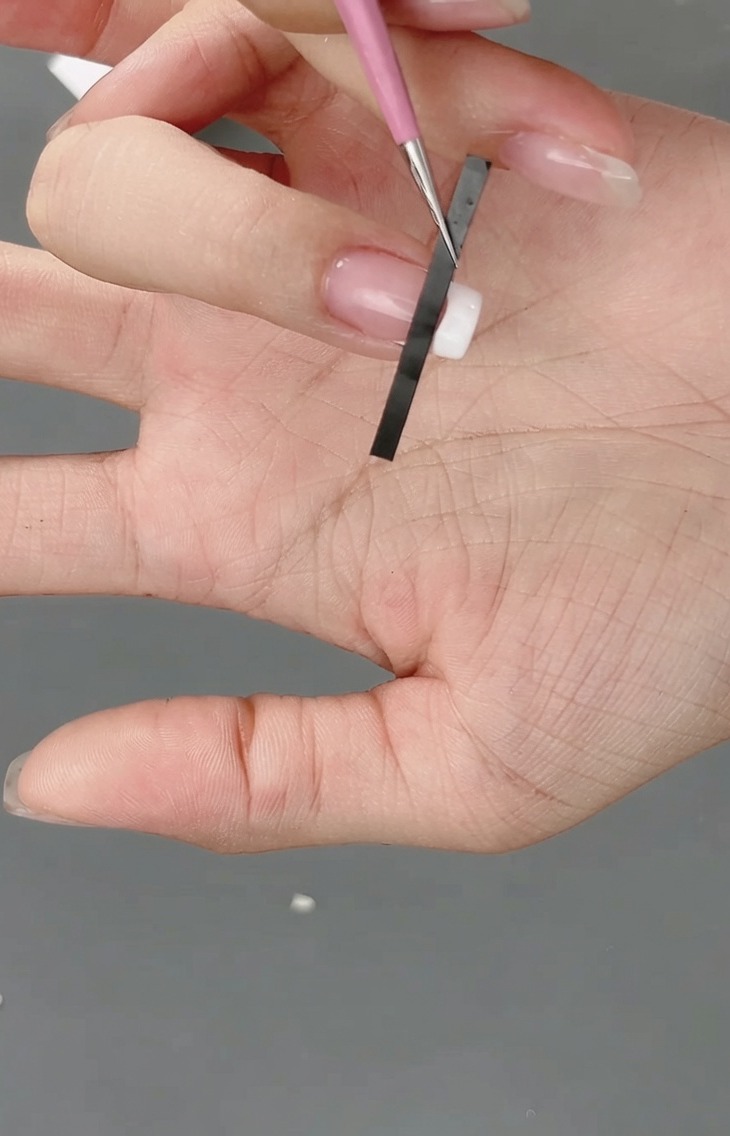 A close-up of a French nail sticker being positioned on a fingernail tip to create a grid guide.