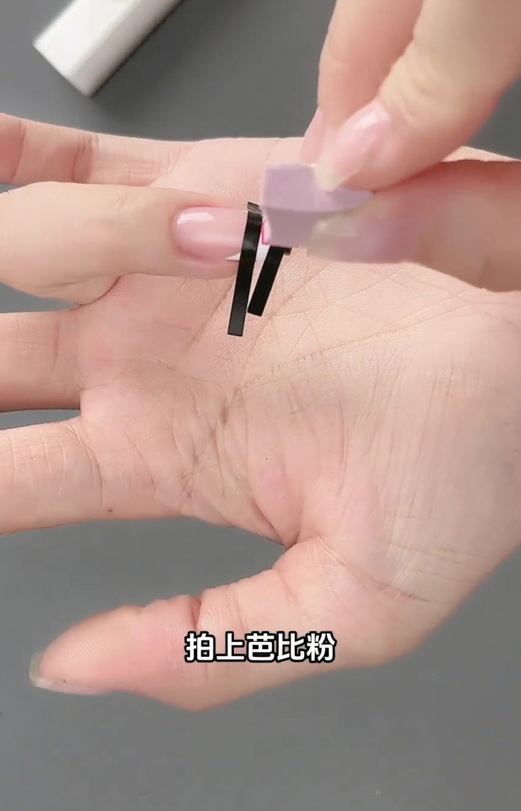 A small sponge tool patting light pink gel polish over the French sticker grid on a nail.