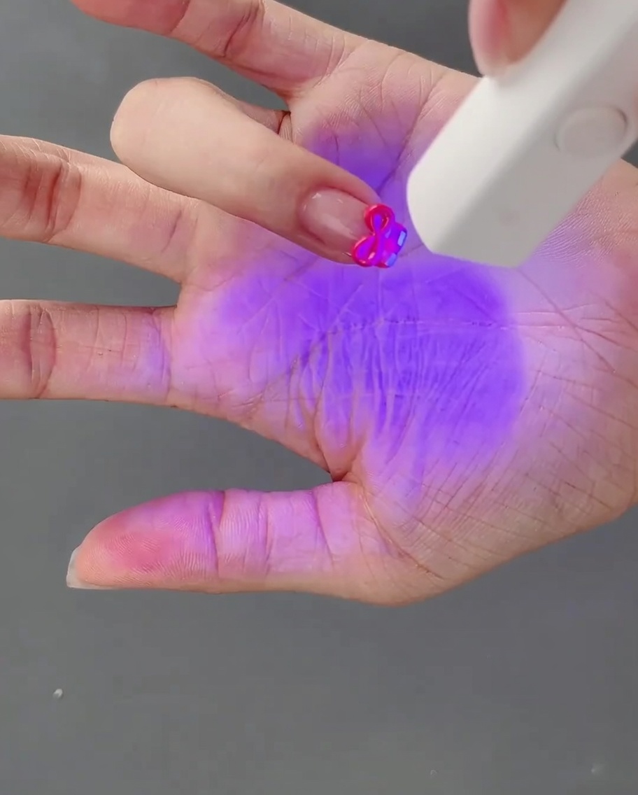 A hand with a freshly crafted 3D gel bow being cured under a UV nail lamp.