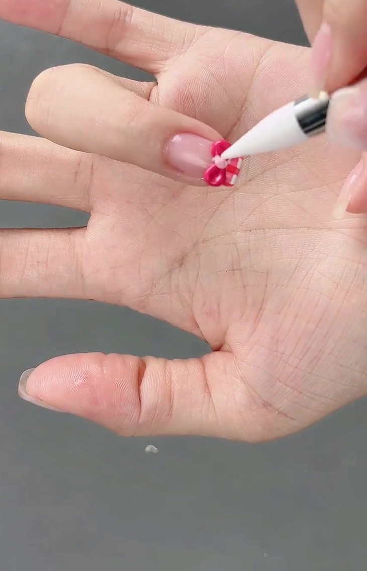 A small light pink gel bead being placed in the center of a 3D bow using a detail brush.