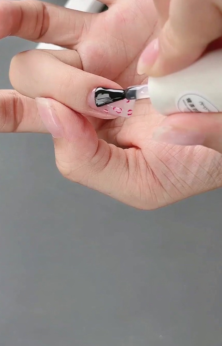 A brush applying a final glossy top coat over the completed French and 3D bow nail design.