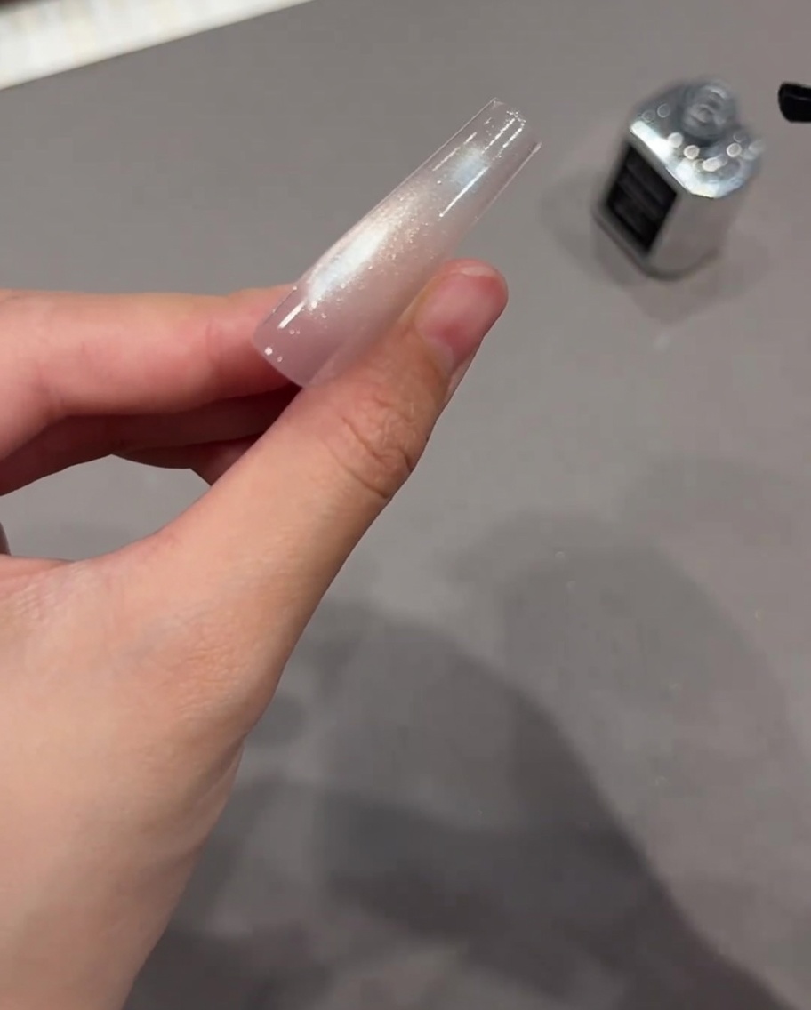 A black nail brush applying clear top coat over a beautifully cured sparkly cat eye gel nail extension.