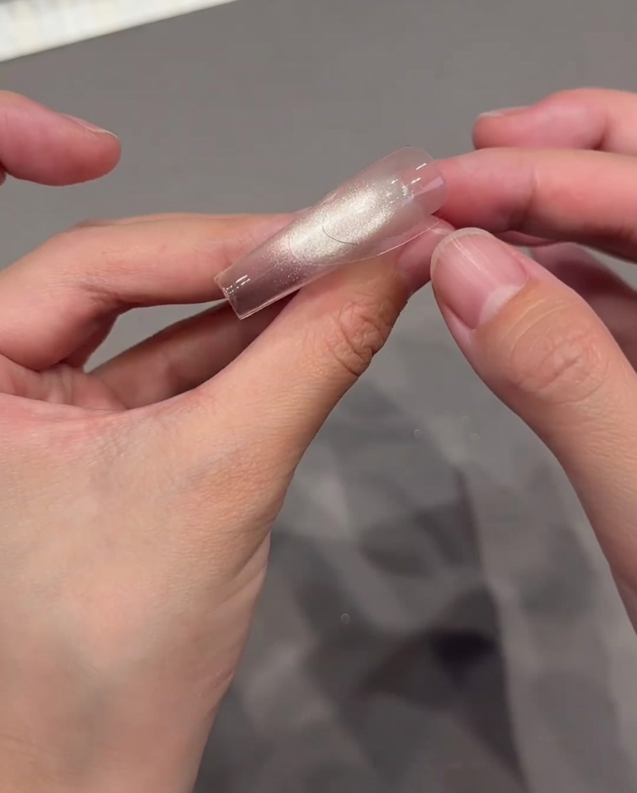 Thumbs carefully placing a transparent curved French tip guide sticker onto a glossy, sparkly nail.