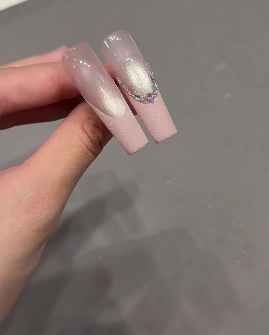 A close-up of a nail with an intricate French design featuring a variety of rhinestones aligned along the tip.