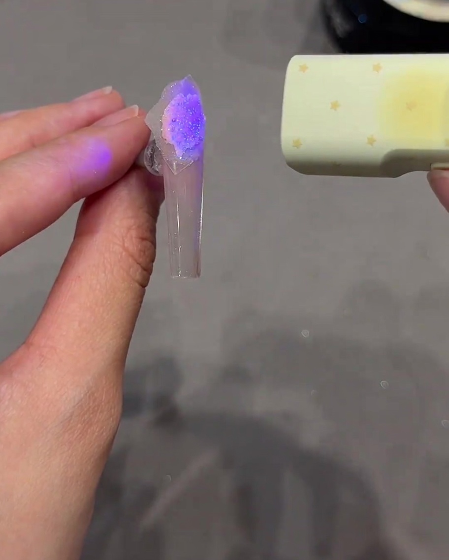 Tweezers pulling a star sticker away from a cured nail, revealing a defined star design.