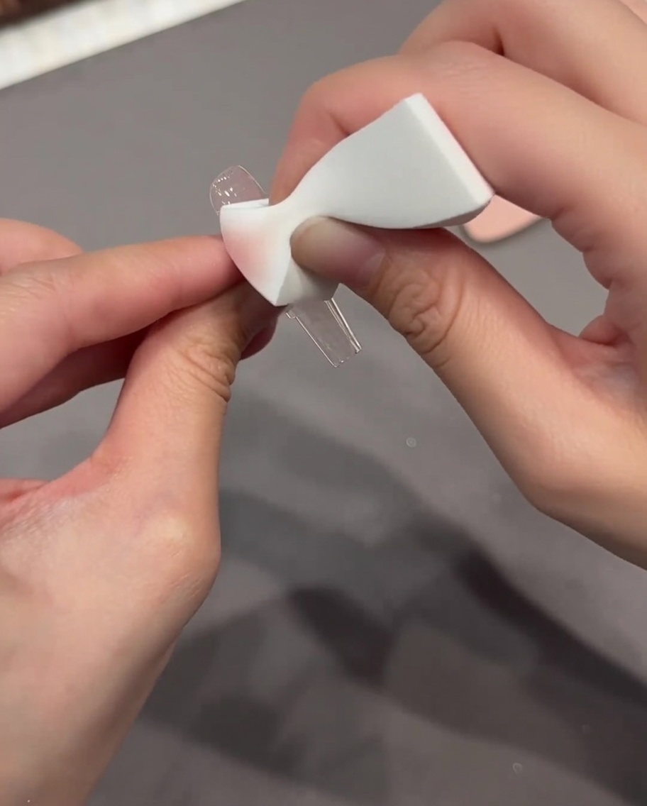 A sponge being used to press and blend a Chrome Heart sticker onto a nail surface.
