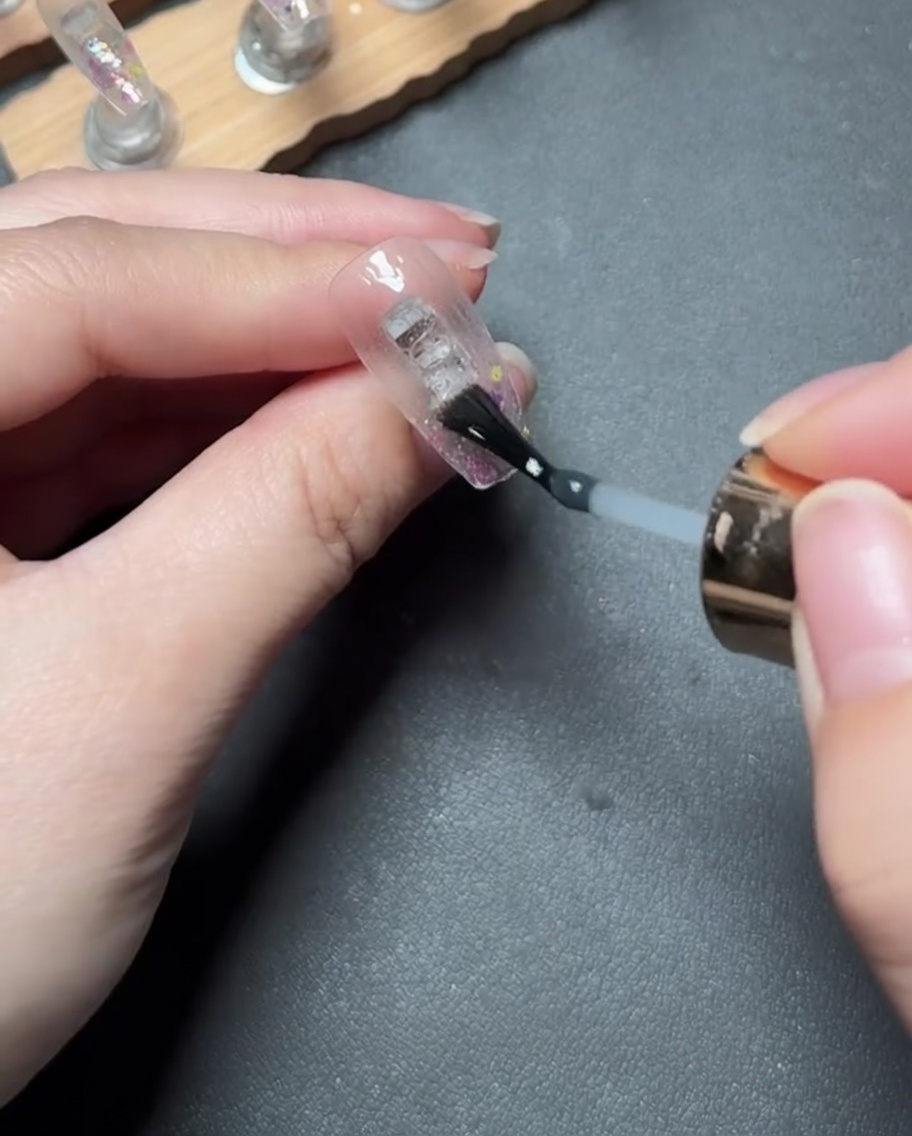 Applying a clear, thick reinforcing gel over the glitter-covered tip of the nail.