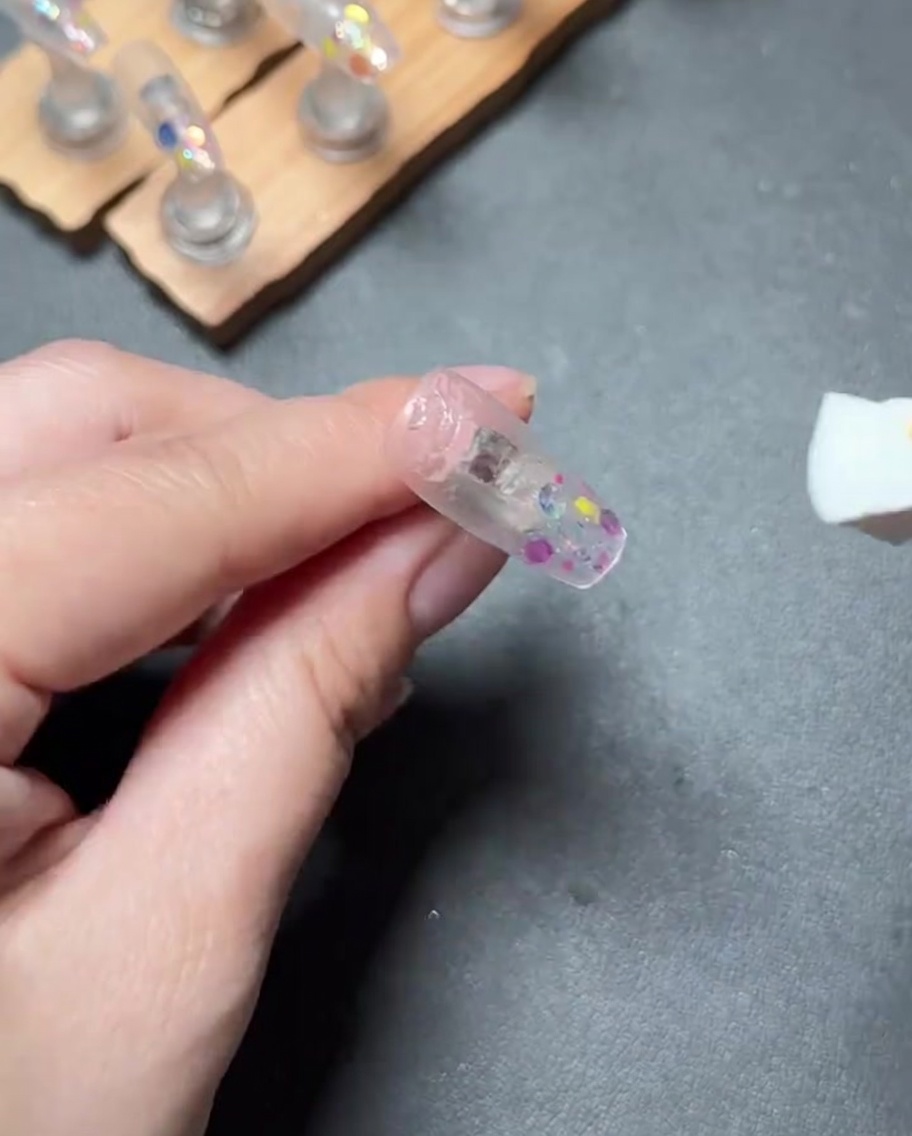 A nail file being used to buff the surface of a press-on nail to create a smooth finish.