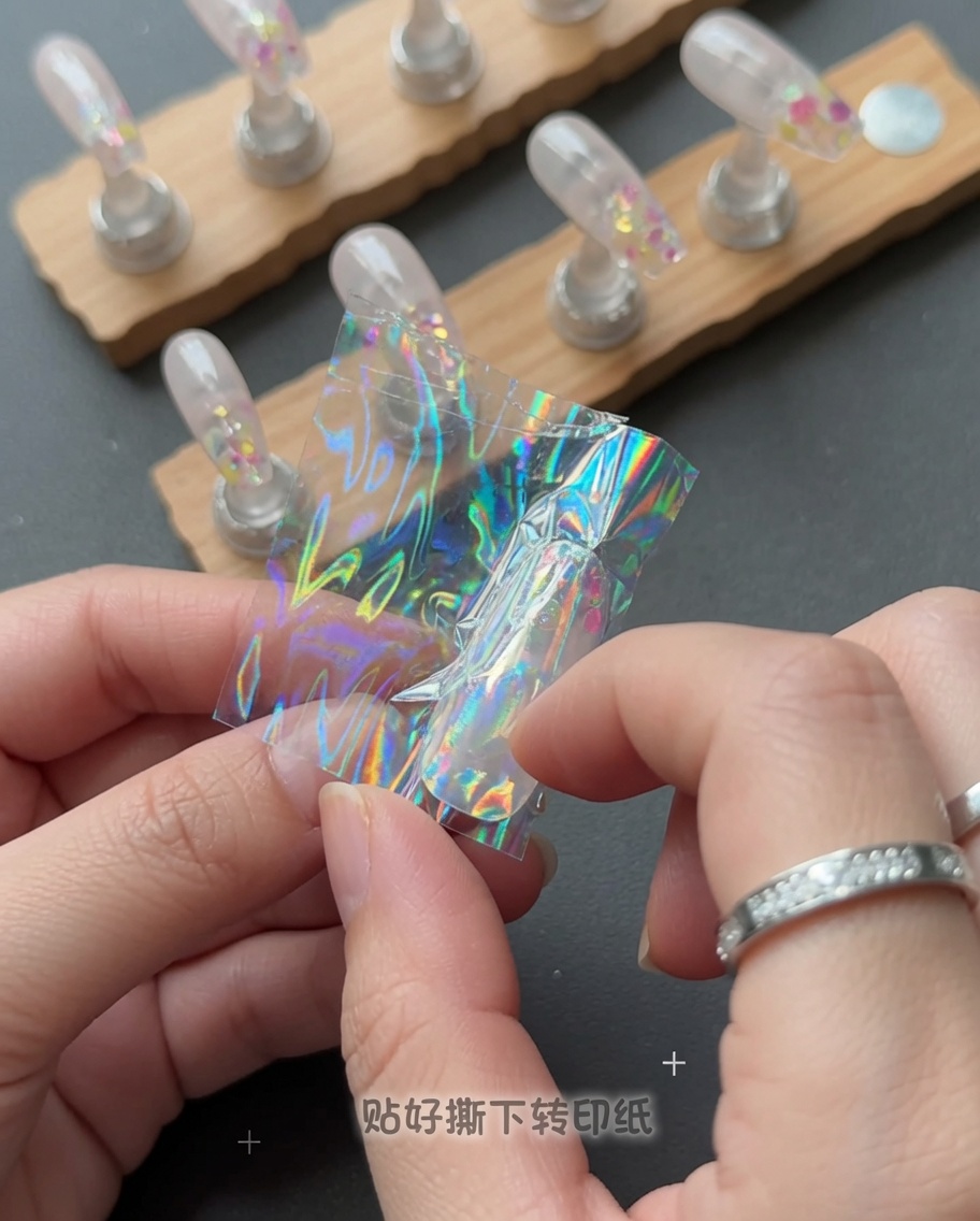 A hand peeling a clear plastic film off a nail to reveal a holographic star design.