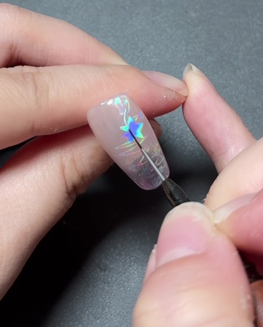 A detail brush painting vibrant colored gel inside a star design on a nail.