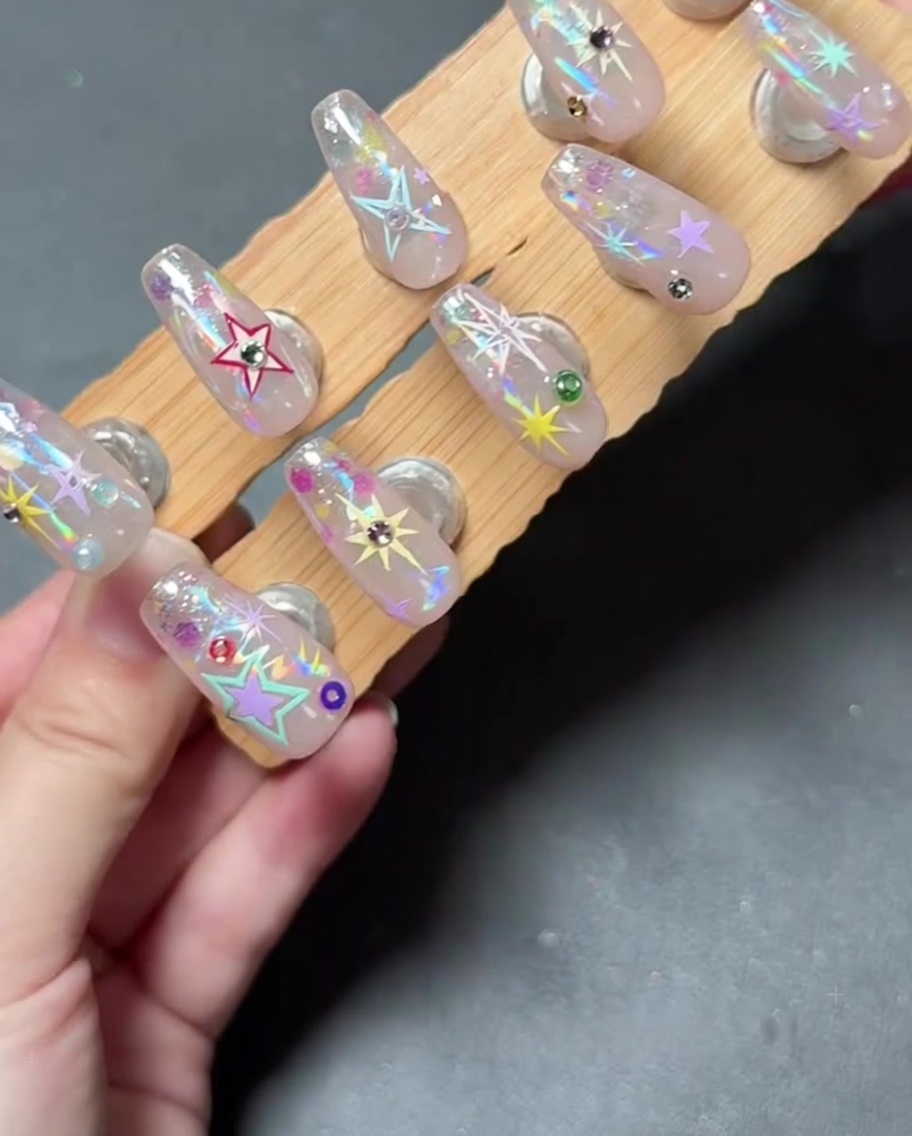 A close-up of a hand placing a small rhinestone on a decorated nail using a tool.