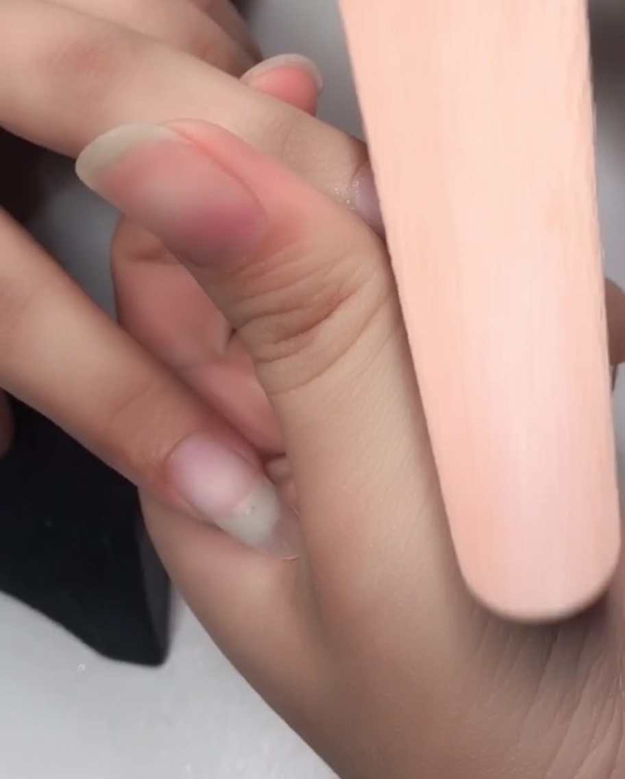 A close-up of a sponge nail file buffing the surface of a nail to prepare it for gel application.