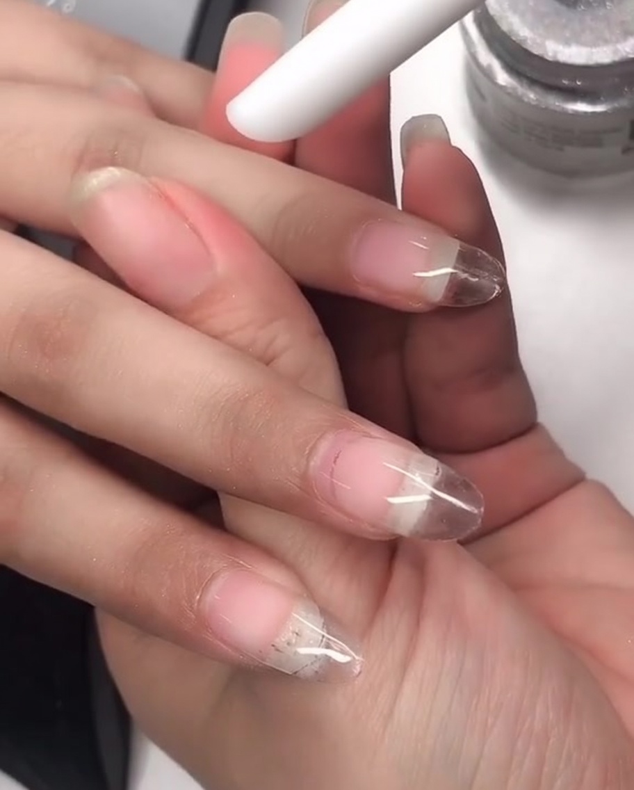 A silicone pen tool being used to rub laser chrome powder onto the surface of a manicured nail.