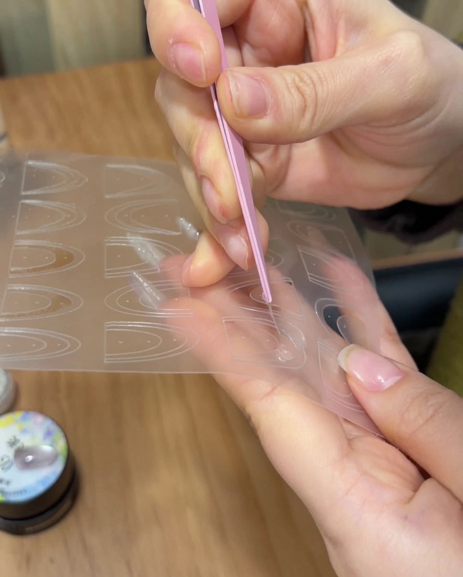 Tweezers placing a thin French manicure sticker guide onto the tip of a manicured nail.