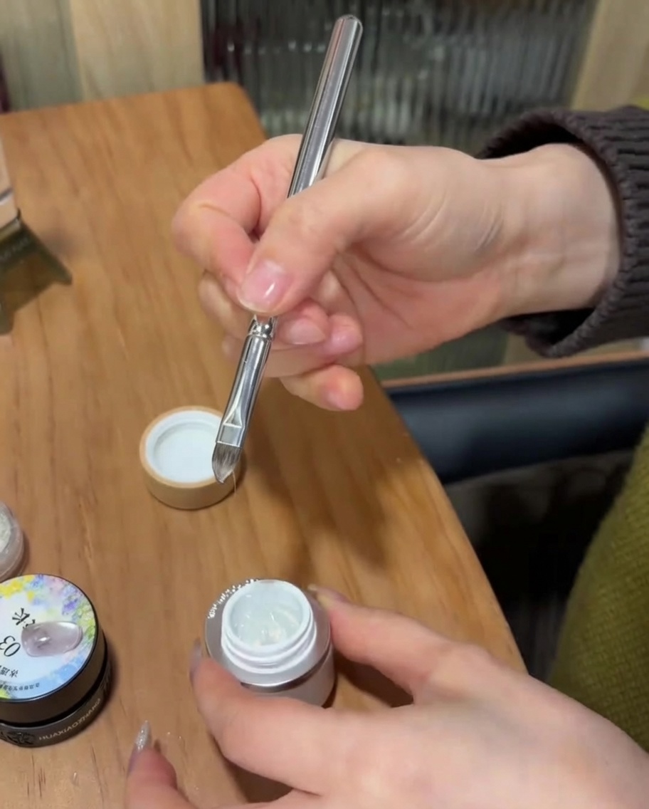 A detail brush applying clear builder gel over the tip of the nail bordered by a French sticker guide.